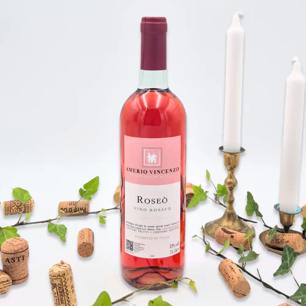 Roseo omgivet af vinkorker, grønne blade og to hvide lysestager på hvid baggrund.