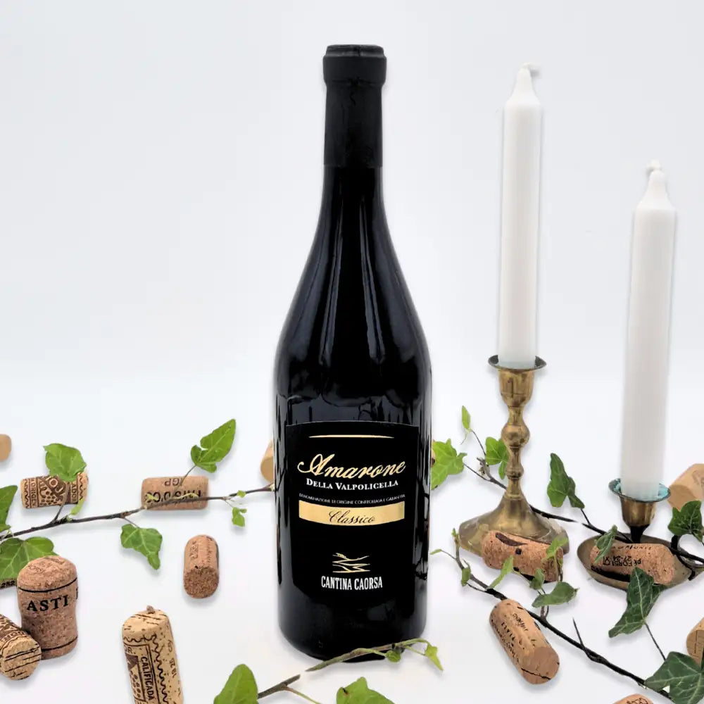Amarone omgivet af vinkorker, grønne blade og to hvide lysestager på hvid baggrund.