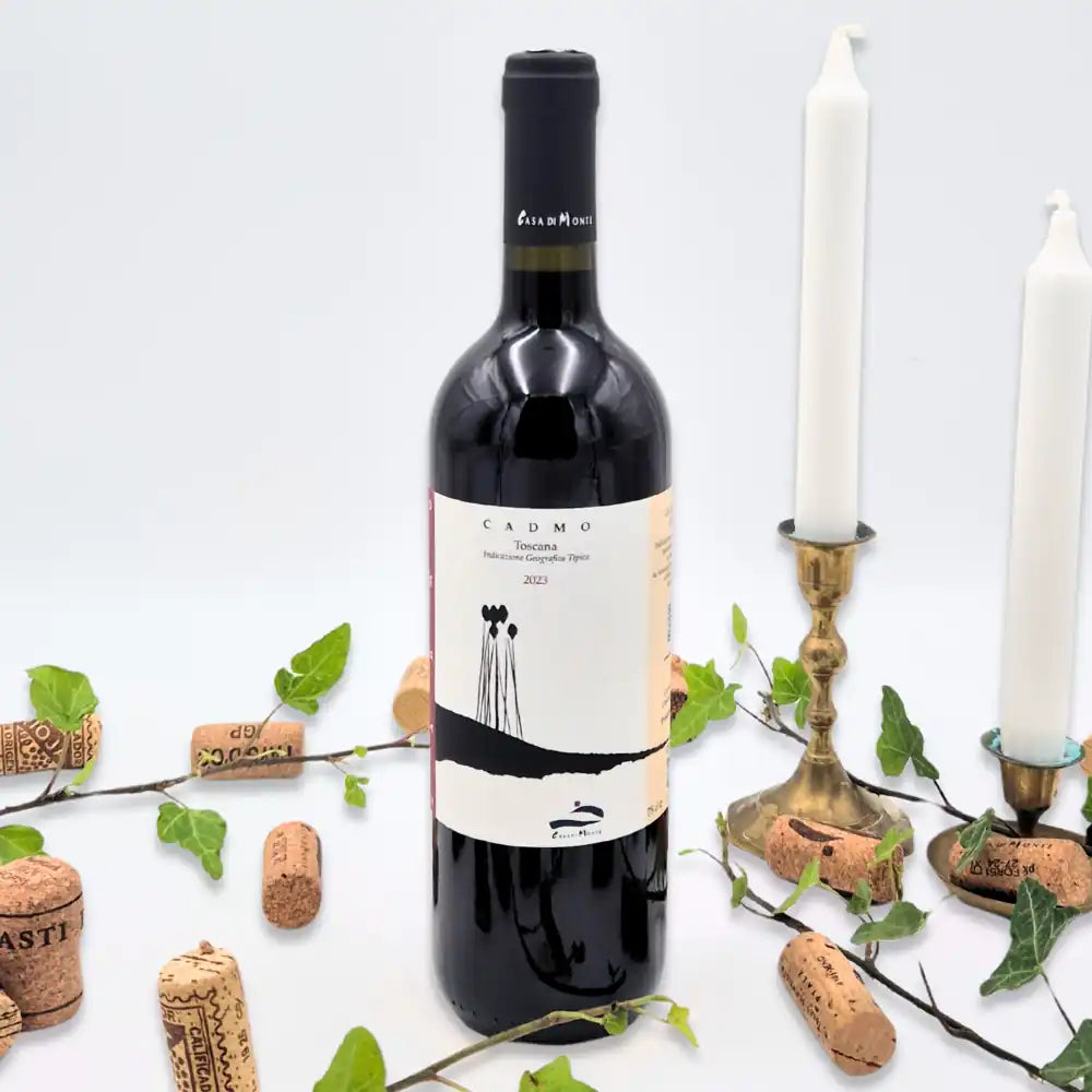 Cadmo omgivet af vinkorker, grønne blade og to hvide lysestager på hvid baggrund.