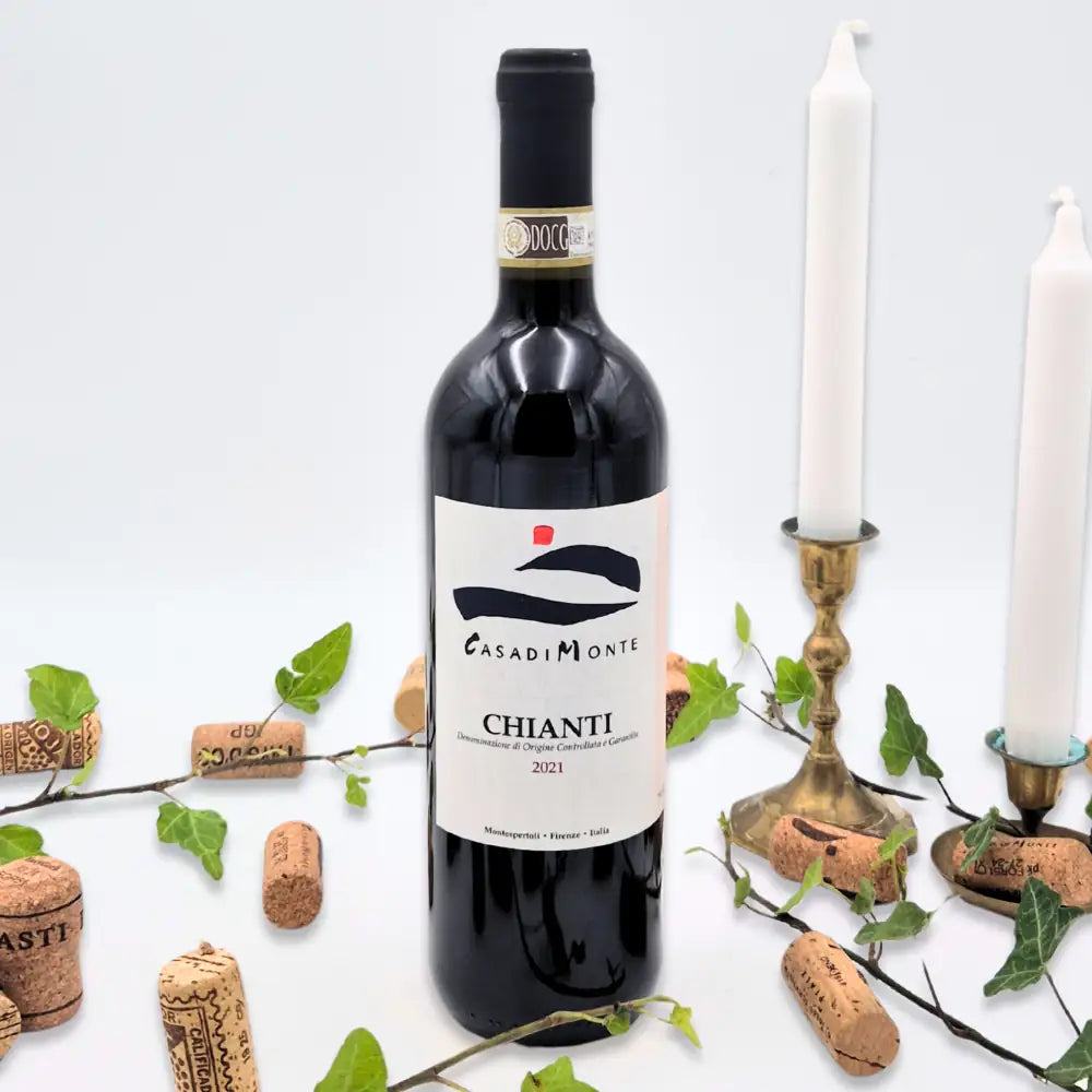 Chianti omgivet af vinkorker, grønne blade og to hvide lysestager på hvid baggrund.