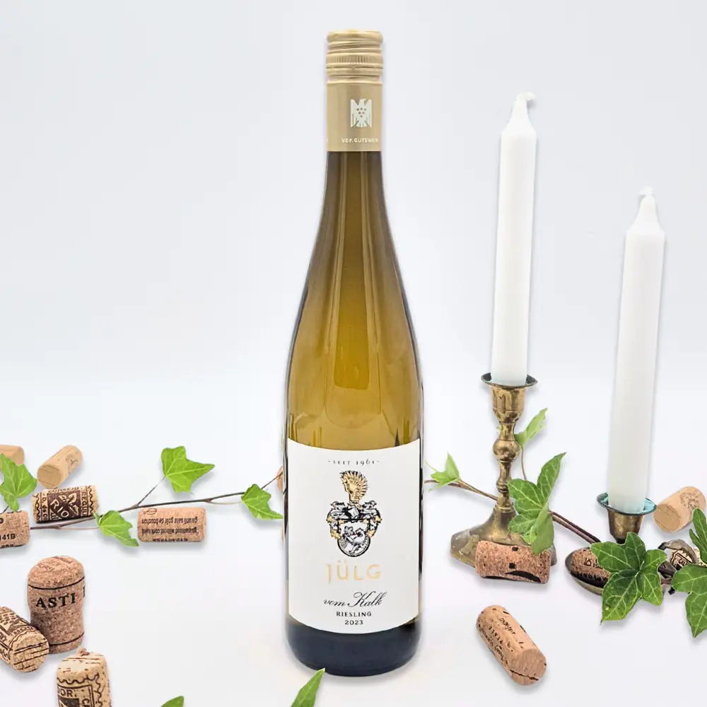 Riesling von kalk omgivet af vinkorker, grønne blade og to hvide lysestager på hvid baggrund.