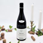 Volnay Vielles Vignes omgivet af vinkorker, grønne blade og to hvide lysestager på hvid baggrund.