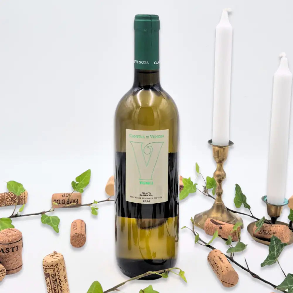 Vignali omgivet af vinkorker, grønne blade og to hvide lysestager på hvid baggrund.