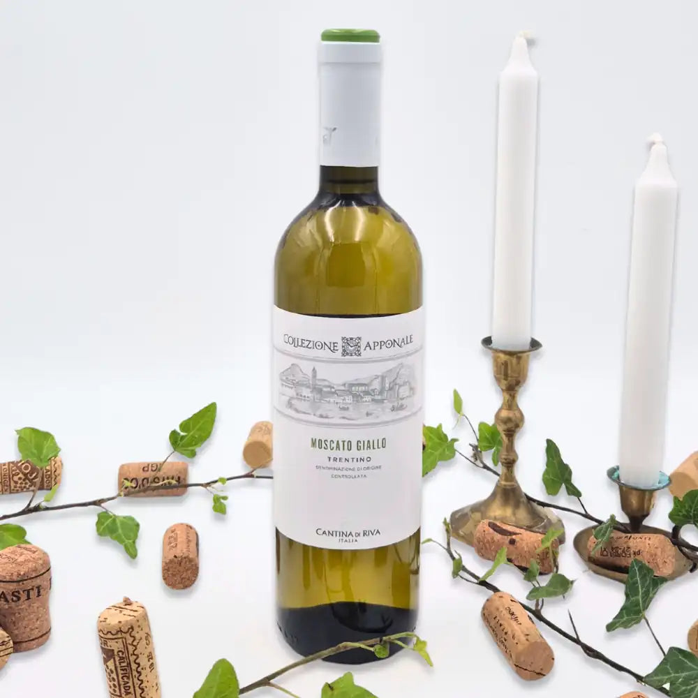 Moscato omgivet af vinkorker, grønne blade og to hvide lysestager på hvid baggrund.