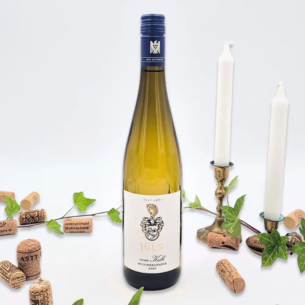 Weissburgunder omgivet af vinkorker, grønne blade og to hvide lysestager på hvid baggrund.