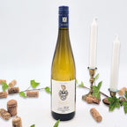 Weissburgunder omgivet af vinkorker, grønne blade og to hvide lysestager på hvid baggrund.